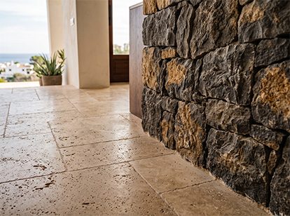 Travertine paving beside a basalt masonry wall; beyond, the terrace and the sea.