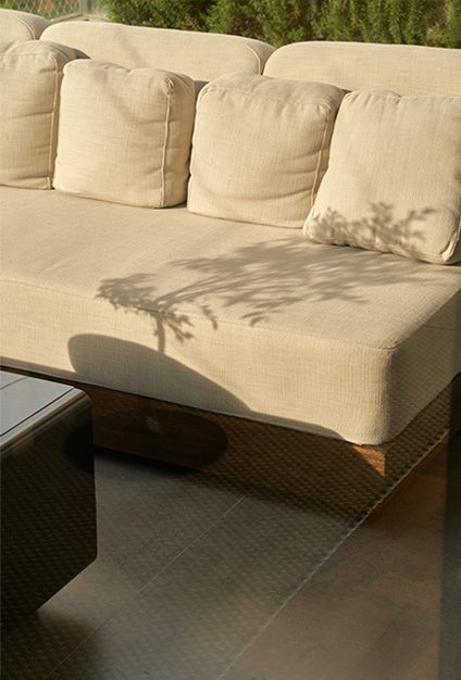 An outdoor sofa upholstered in ecru, with the shadow of an olive tree cast across the cushions.
