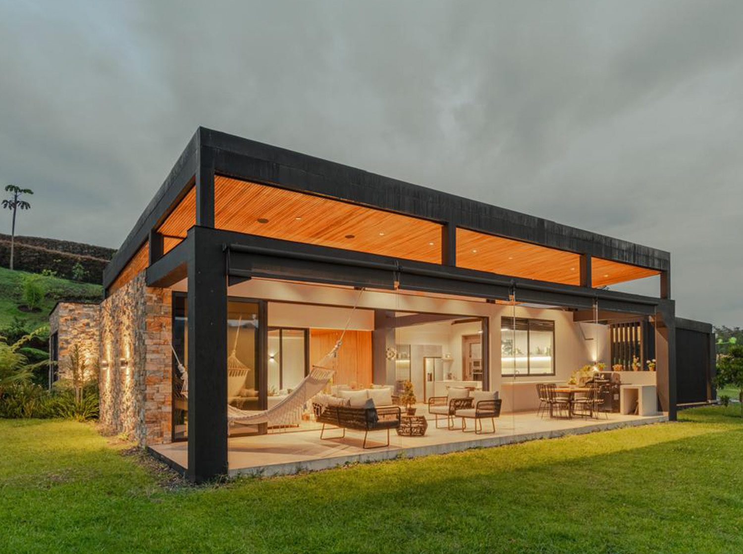Casa LM: a flat-roofed volume with a dark frame and a timber ceiling, set on open meadowland.